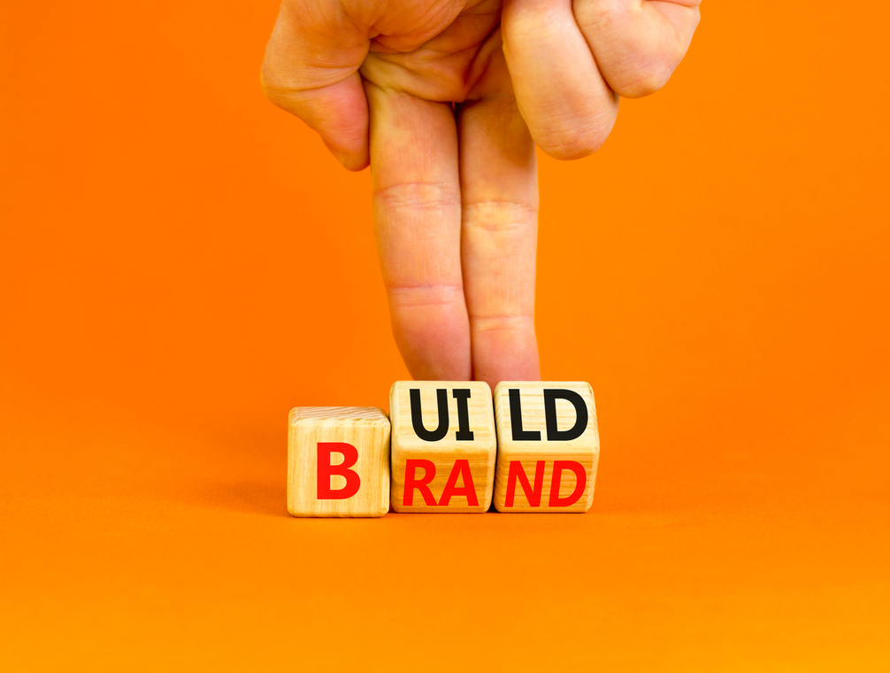 Build your brand symbol. Concept words Build brand on wooden cubes. Businessman hand. Beautiful orange table orange background. Build your brand and business concept. Copy space.